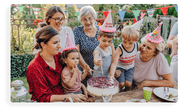 A family at a child's birthday party gathered around a birthday cake while the birthday boy cuts the cake.