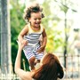 A mother lifting up her child in the air at the park. The child is smiling and laughing