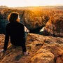 A woman sat on a rocky cliff overlooking the beautiful cavernous terrain with the golden sun setting in the background.