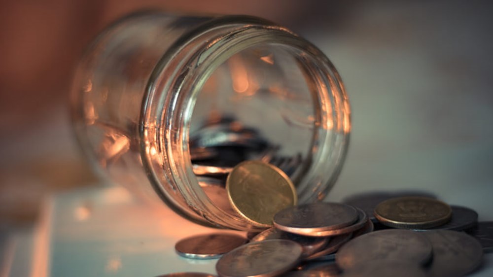 A money jar lying on its side with coins pouring out of it.