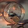 A glass money jar tipped over with a handful of copper coins spilling onto a countertop. 