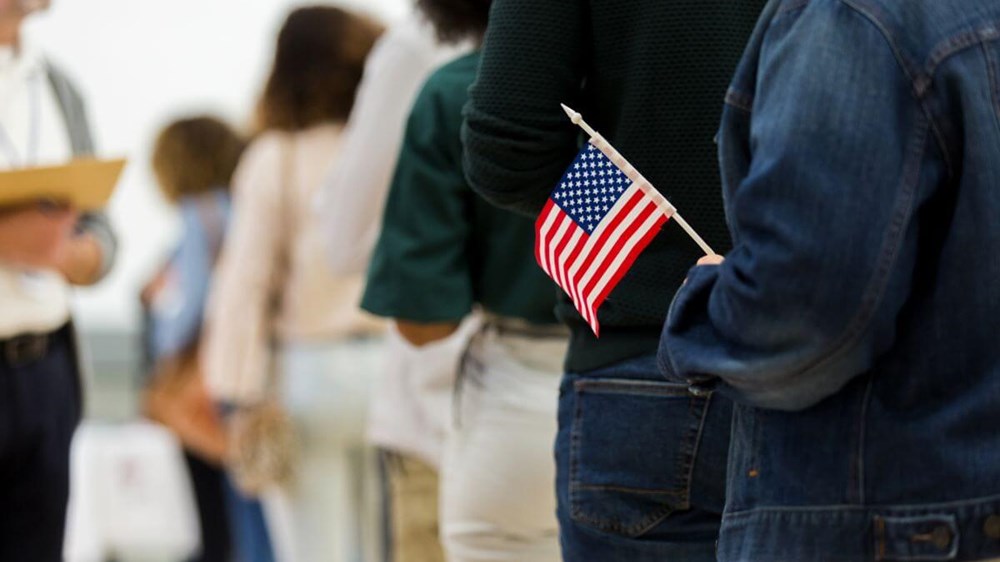 People in a queue (waiting to vote) with a person holding a small American flag.