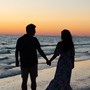 A couple walking along a beach at sunset holding hands.
