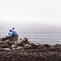A couple sitting on a pile of big rocks overlooking a scenic view of the sea.