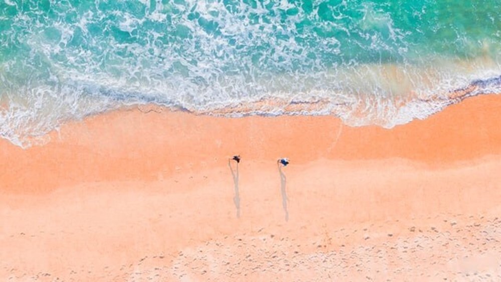 Couple walking along a beach from above | Wealthify