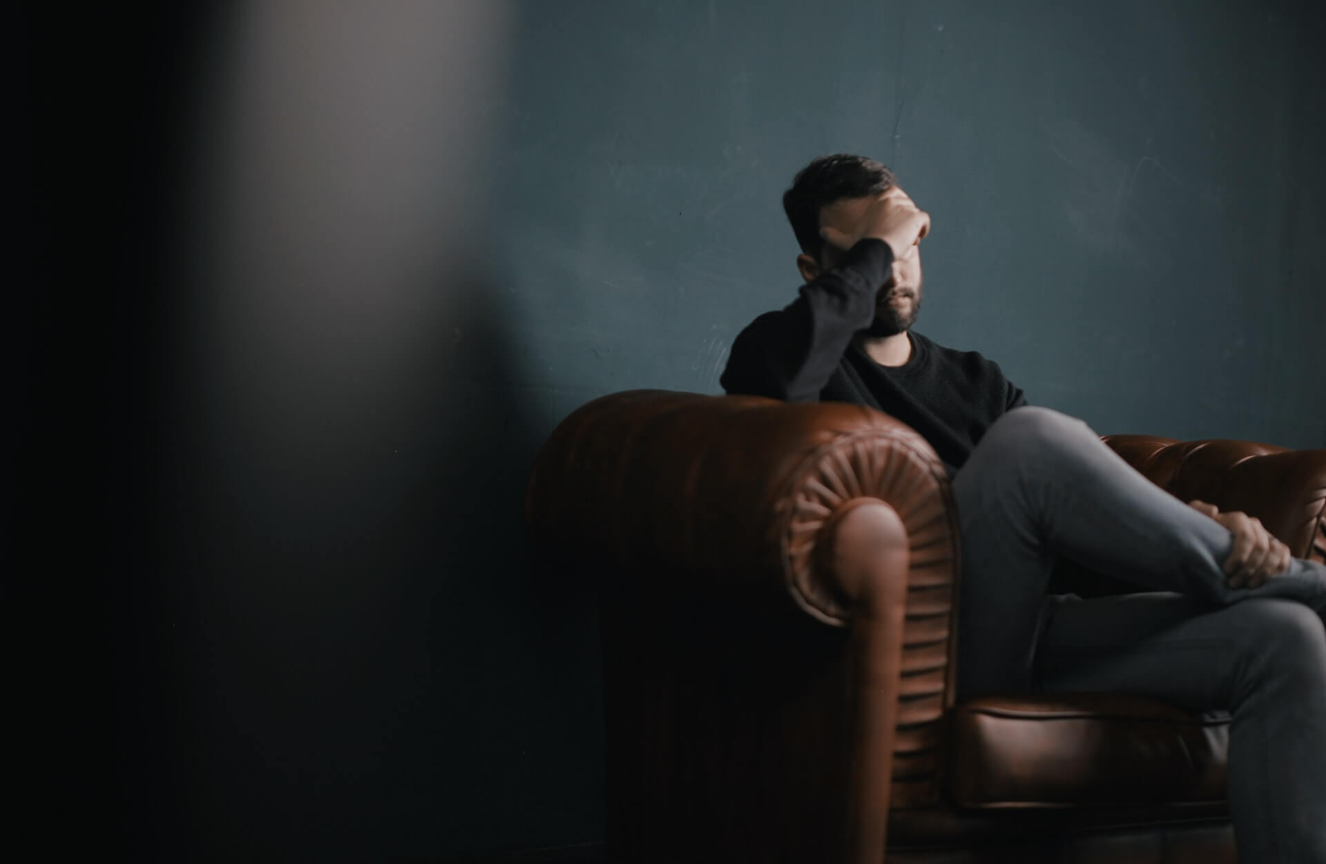 Stressed man sitting on sofa with hand on face