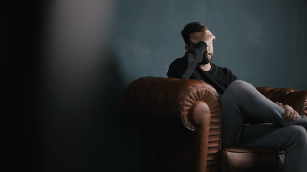 Stressed man sitting on sofa with hand on face