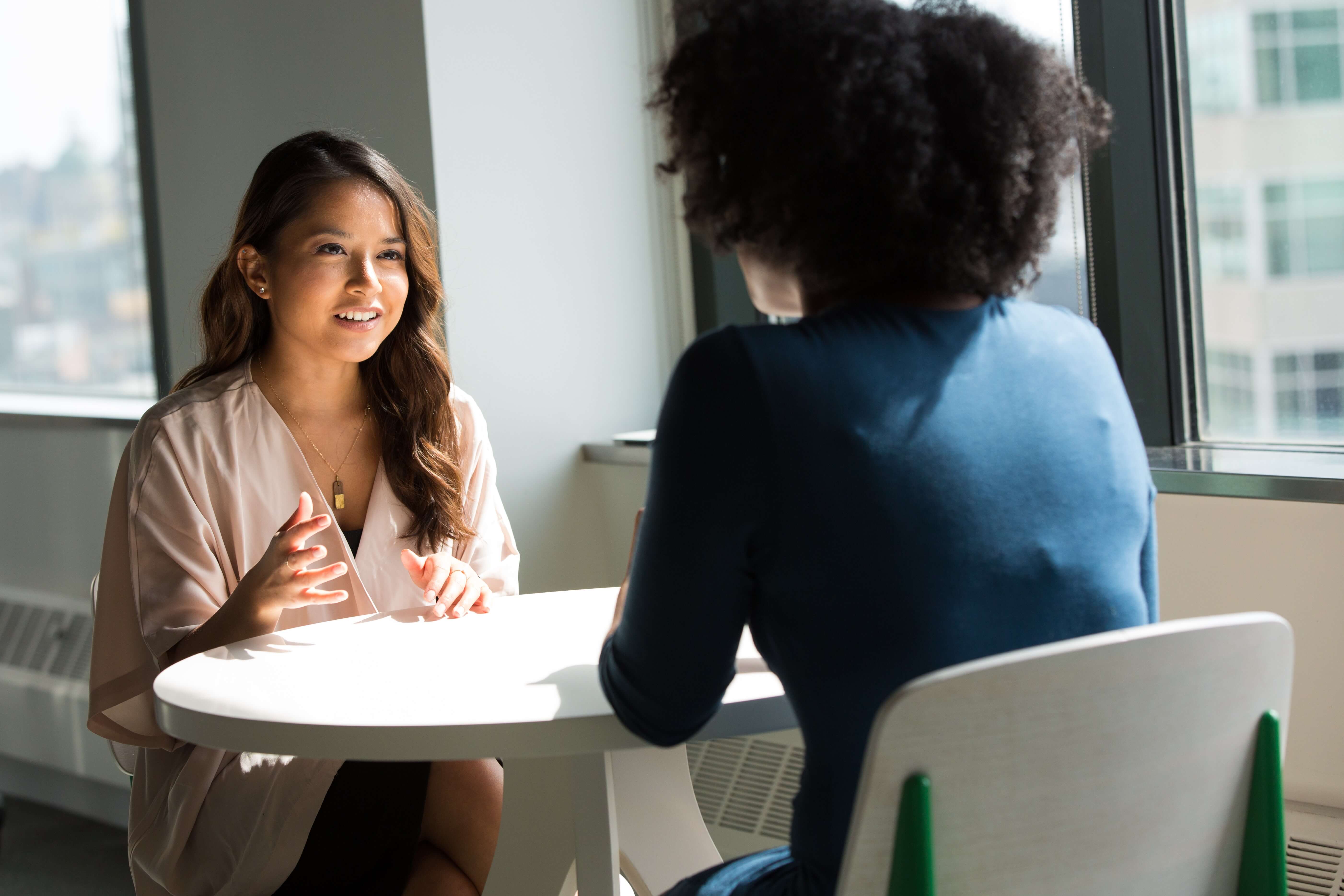 Two woman speaking as they sit across a table from each other