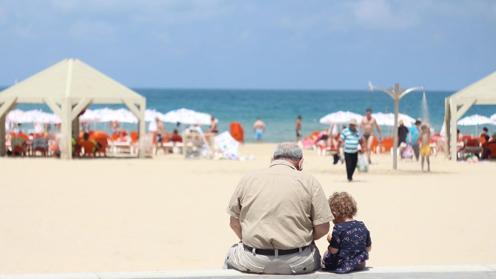 Grandad and grandchild sitting on wall facing beach