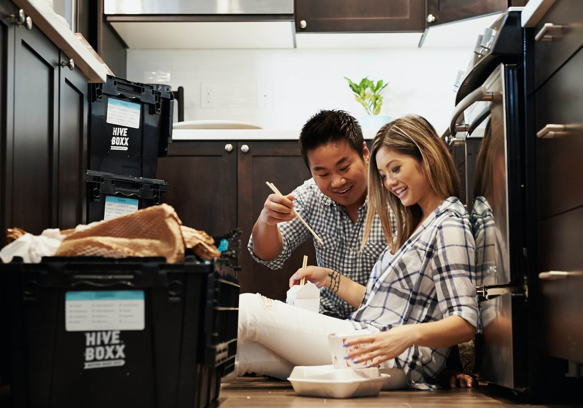 Couple sitting on the floor eating while surrounded by moving boxes