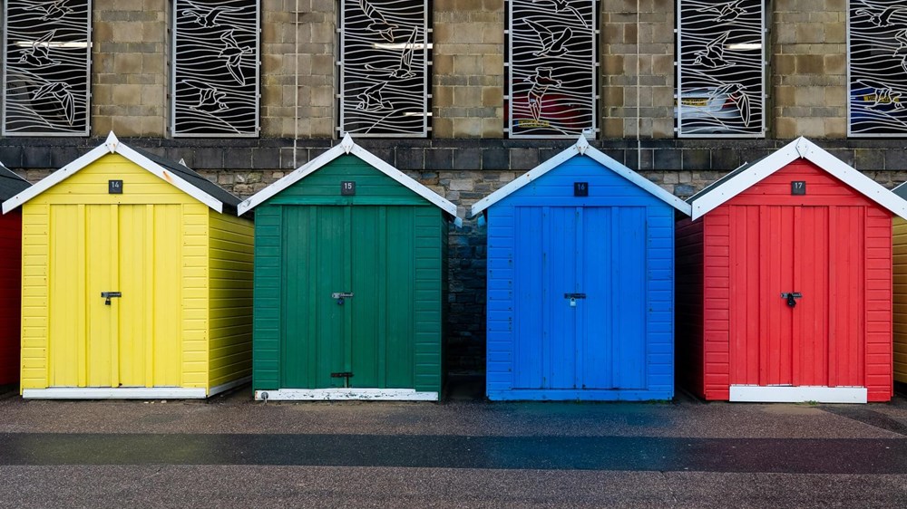 four different coloured sheds standing next to each other - from left to right the sheds are yellow, green, blue and red | wealthify.com