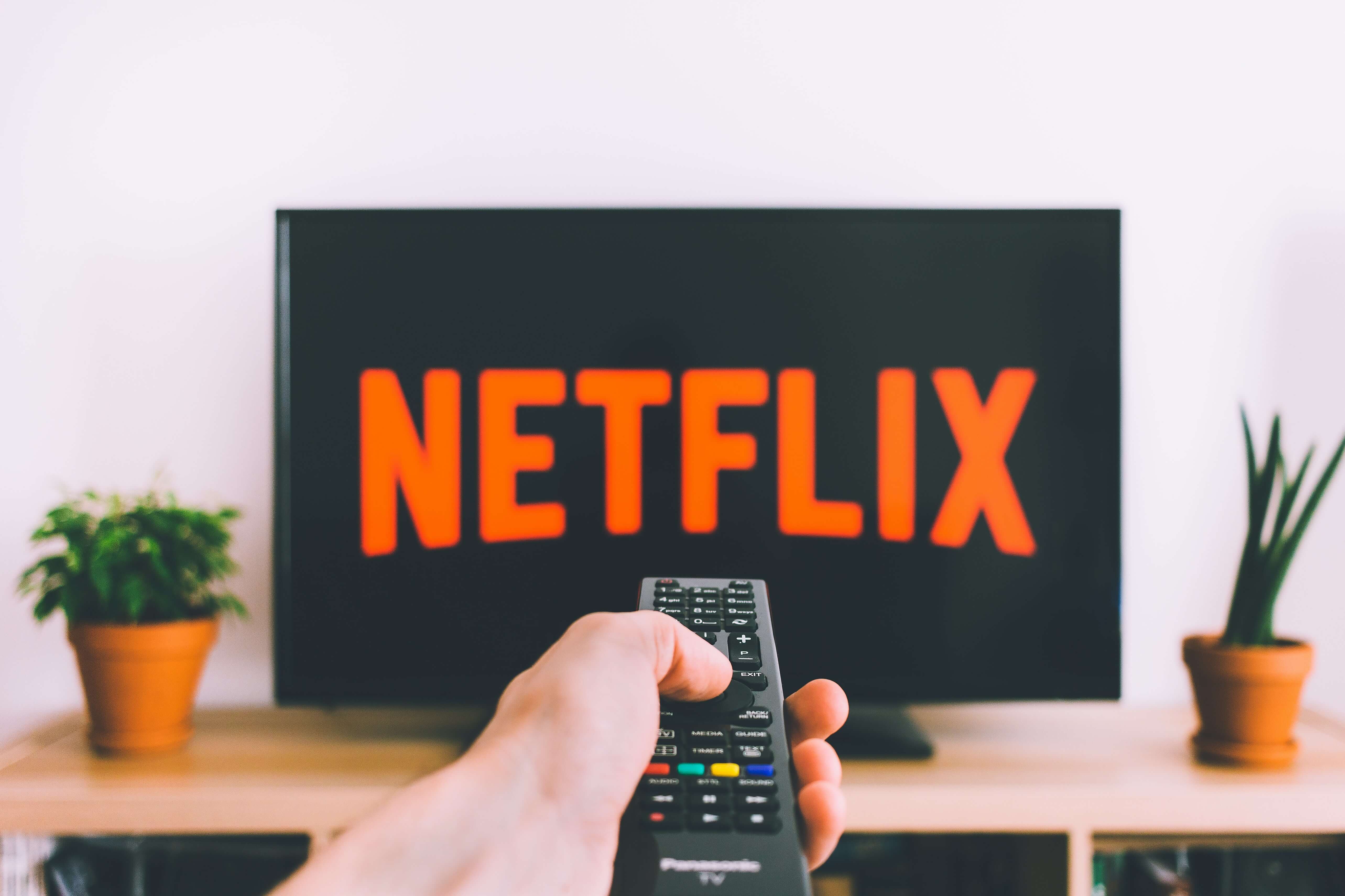 Hand holding up remote to television screen displaying the Netflix logo