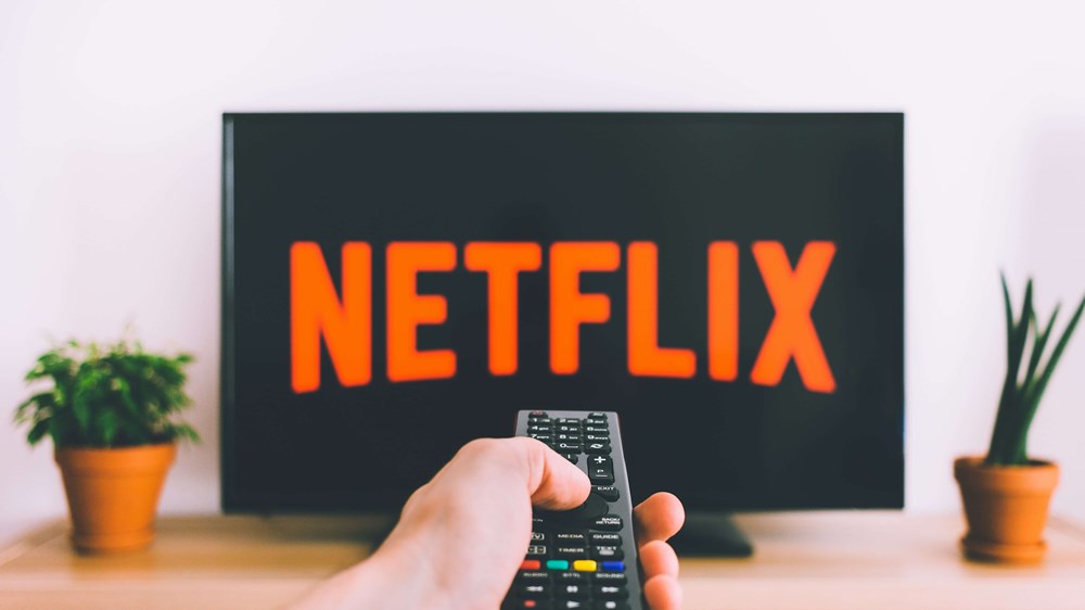 Hand holding up remote to television screen displaying the Netflix logo