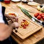 A chef in a white shirt and black apron cutting baby plum tomatoes on a wooden chopping board with an assortment of vegetables next to it | wealthify.com