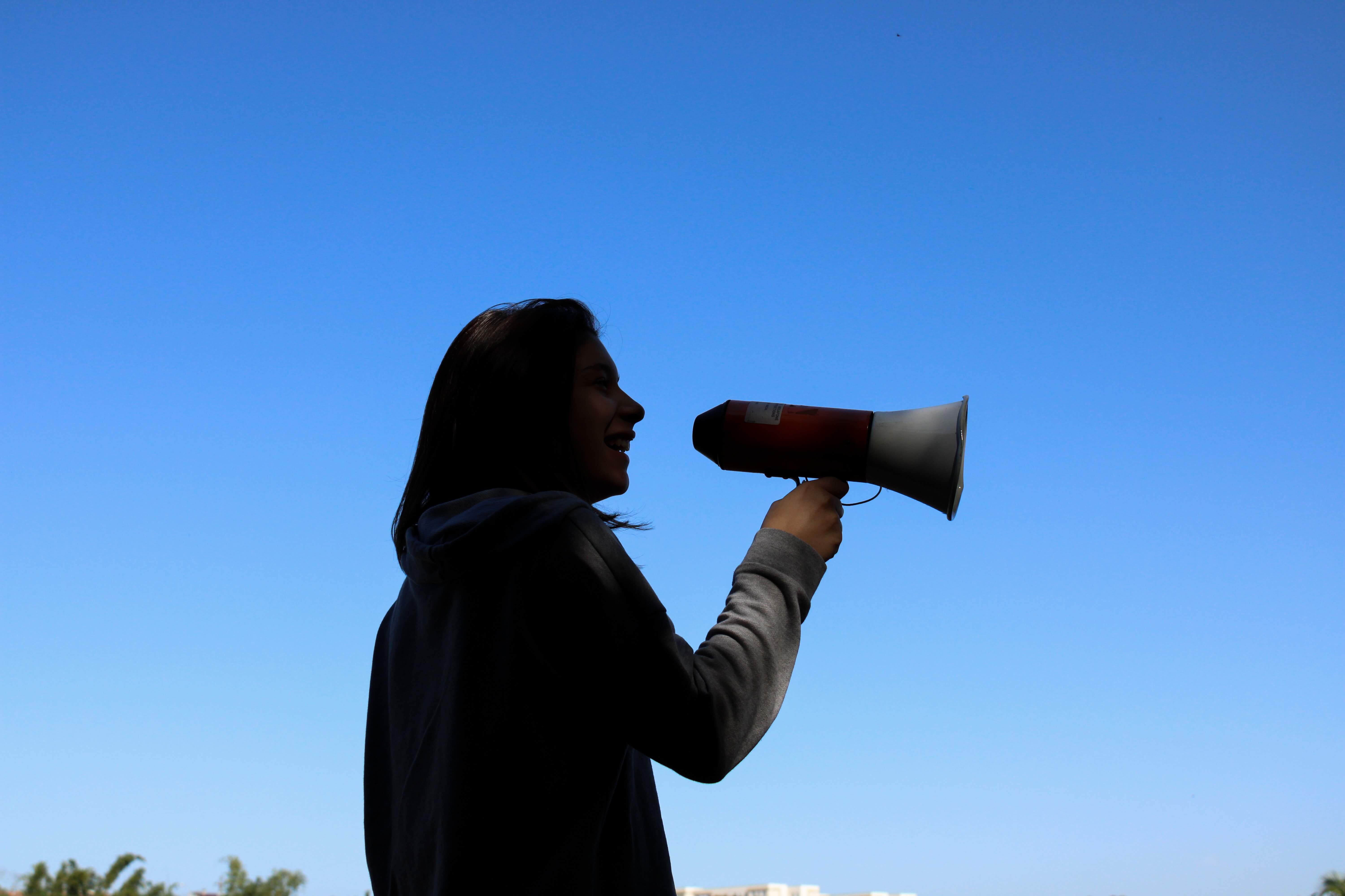 Woman speaking into a megaphone in front of a blue sky