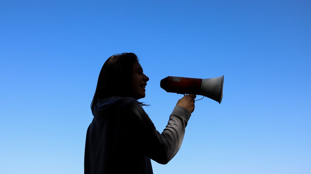 Woman speaking into a megaphone in front of a blue sky