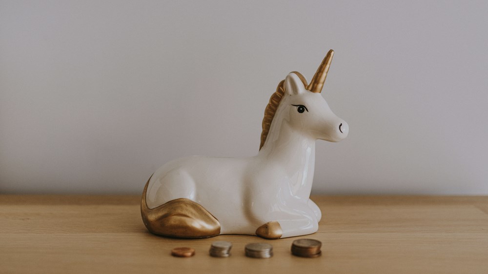 Unicorn money box with pile of coins in front of it