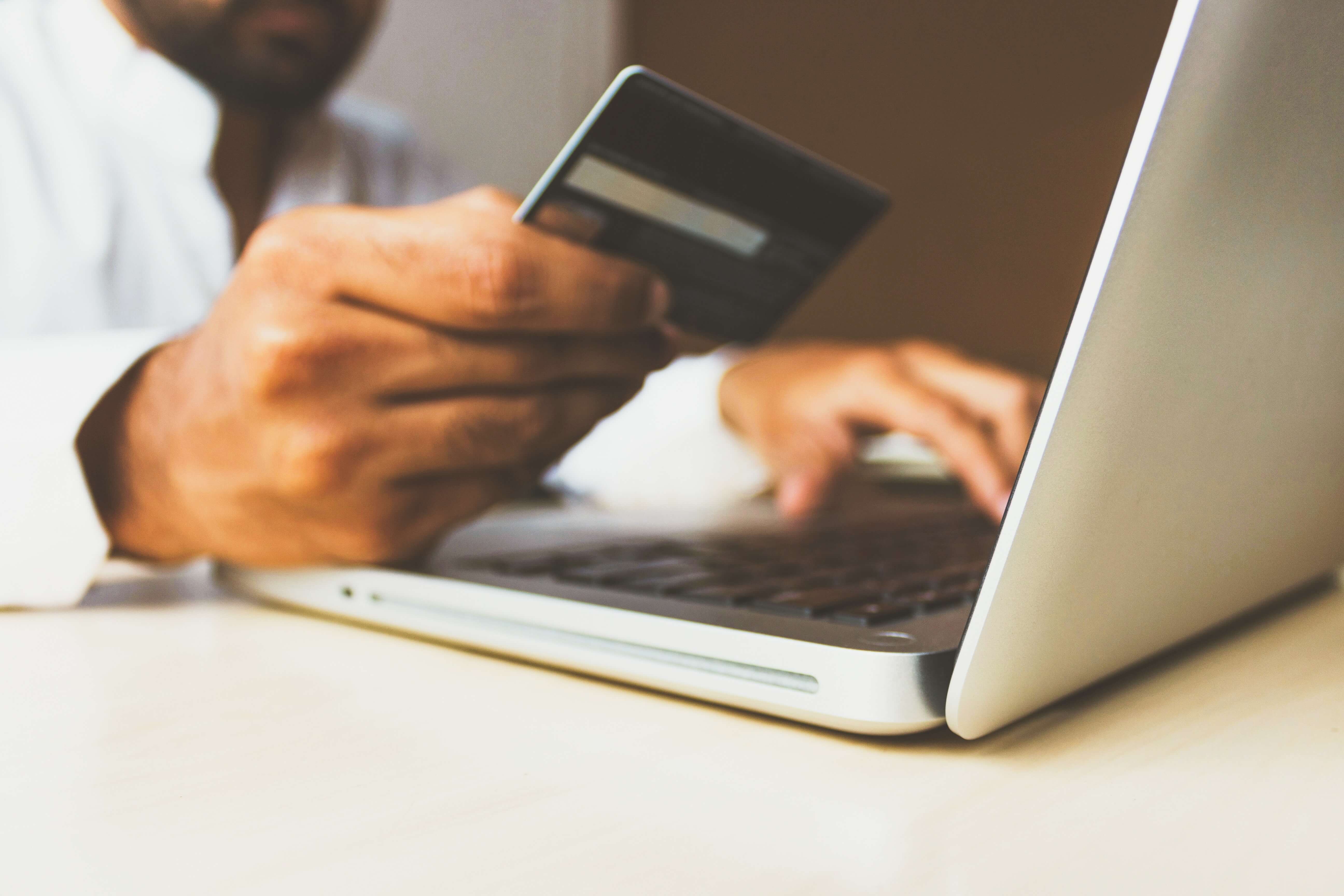 Close up of hands holding debit card and typing on a laptop