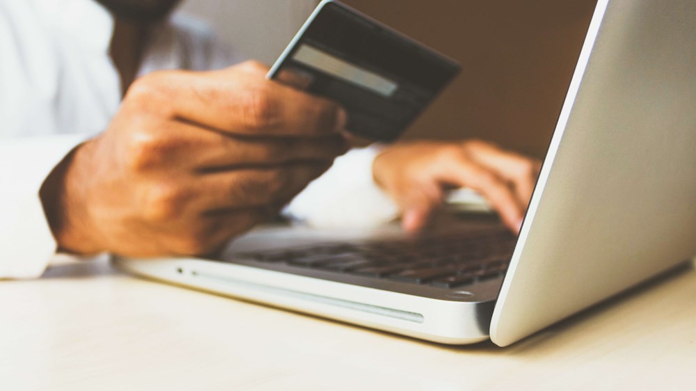 Close up of hands holding debit card and typing on a laptop