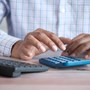 A man sat a desk typing on a calculator