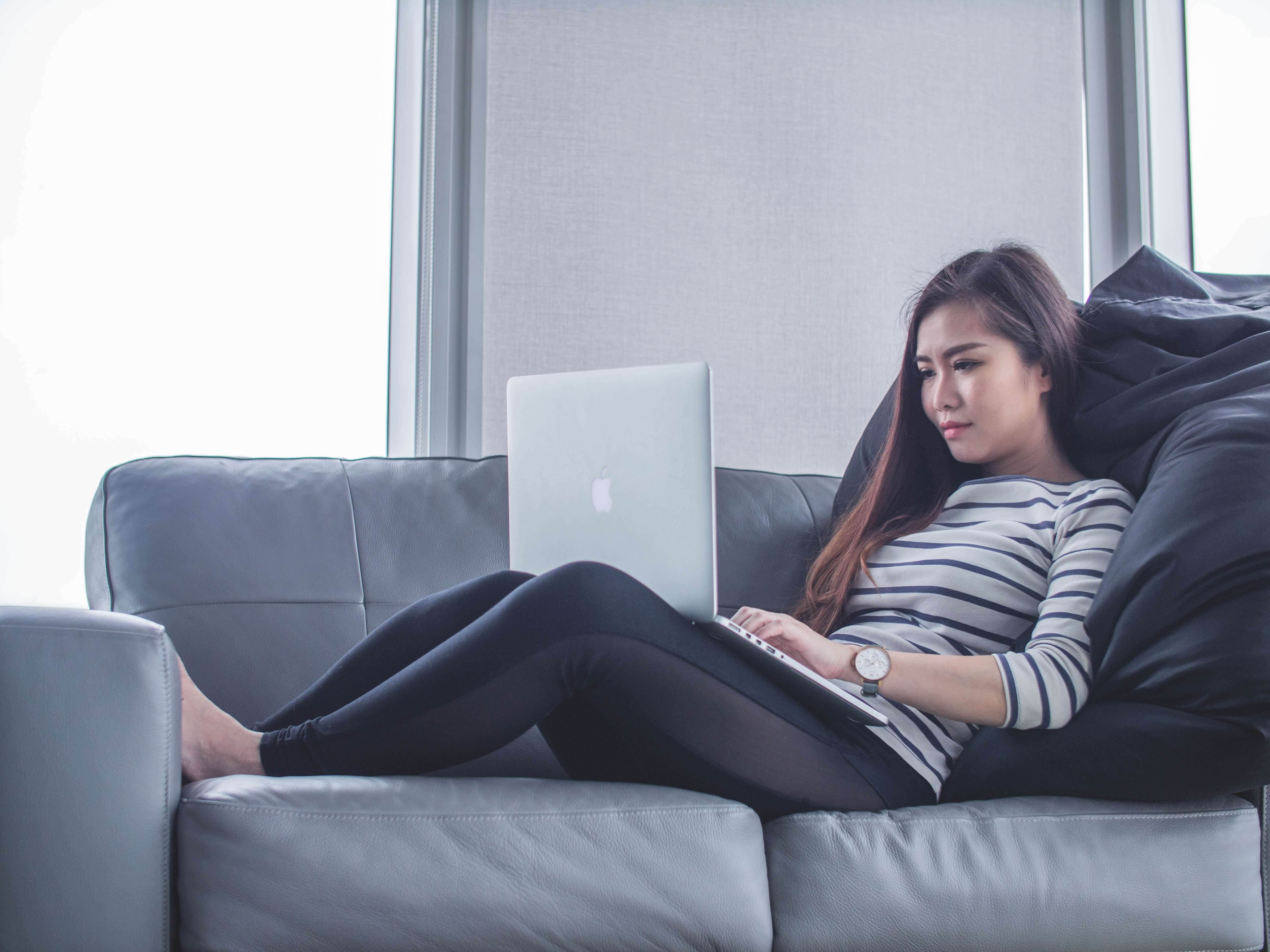 Woman laying on sofa using a laptop