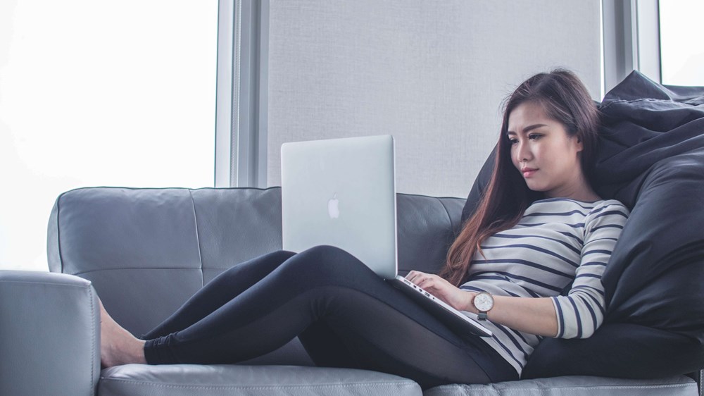 Woman laying on sofa using a laptop