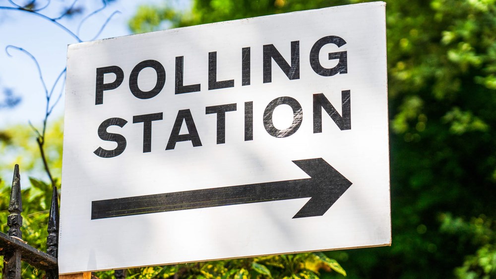 Photograph of a sign that says 'polling station' with greenery in the background