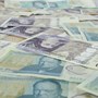 British pound bank notes spread across a table. Some with the value of five pounds, others with a value of twenty pounds.