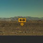 A landscape of a desert with a yellow road sign with arrows pointing both left and right.