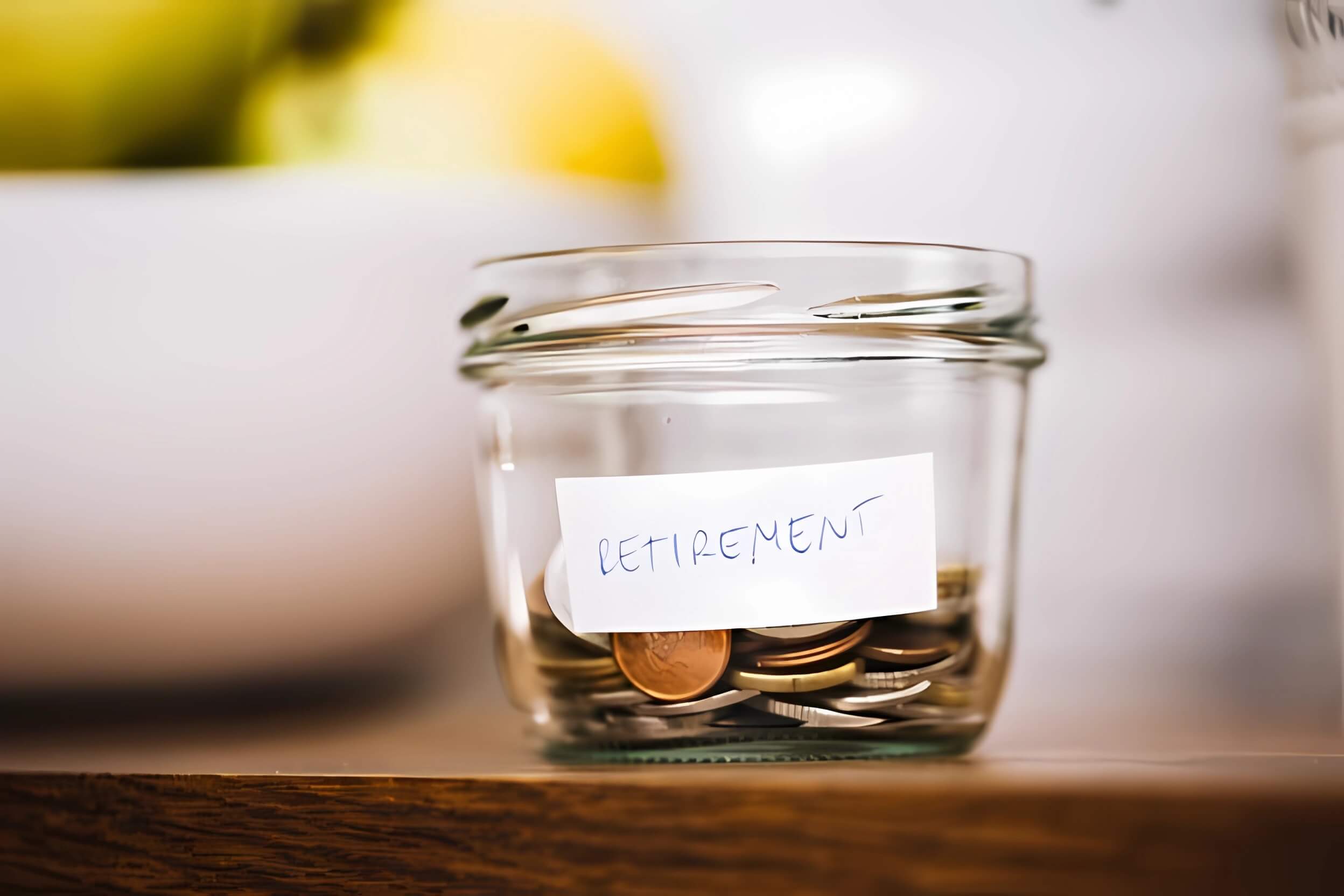 A small glass pot containing change resting on a table. On the pot is a label that reads 