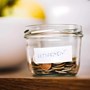 A small glass pot containing change resting on a table. On the pot is a label that reads "RETIREMENT"