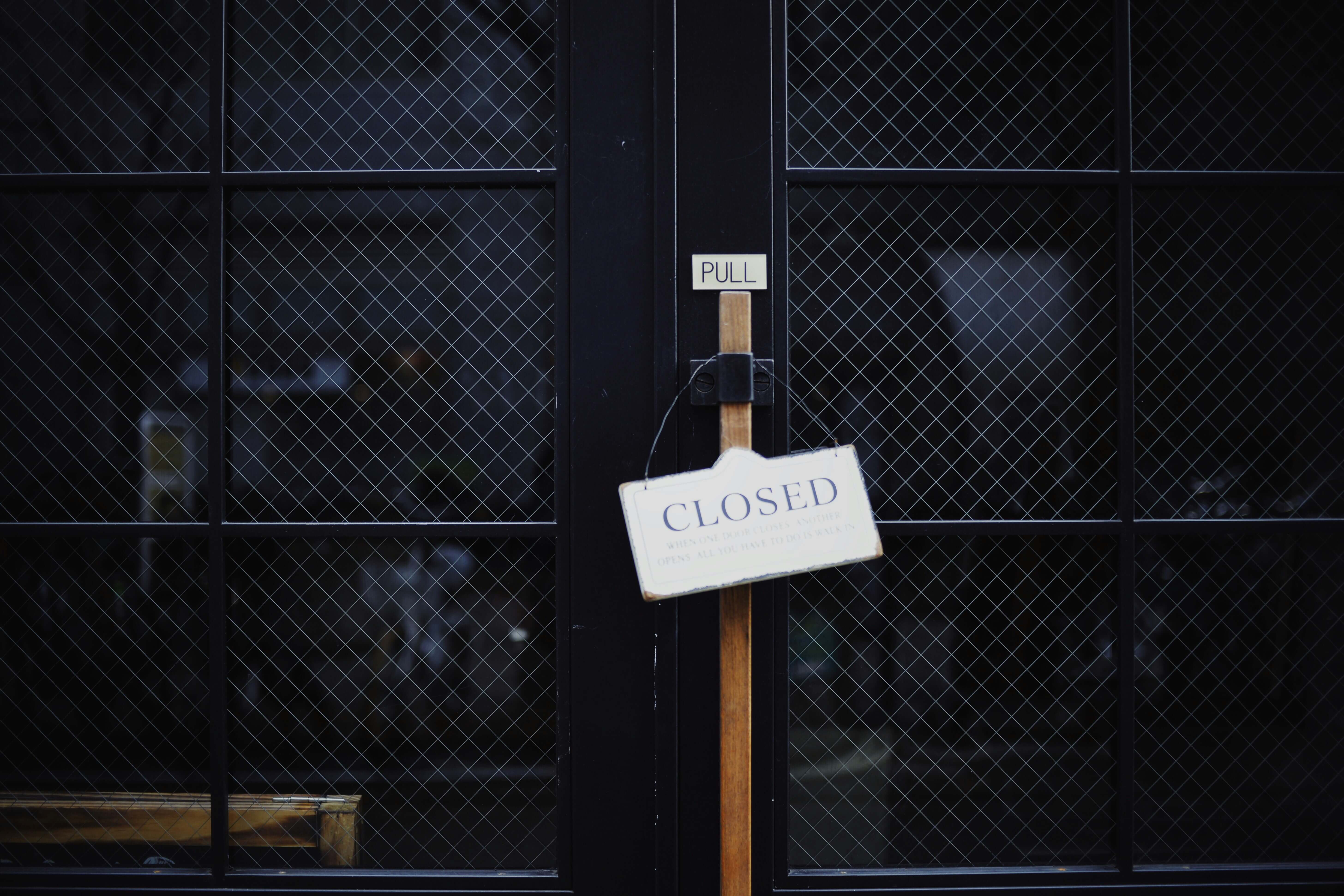 A photograph of two doors with a shop sign that reads Closed on the door handle.