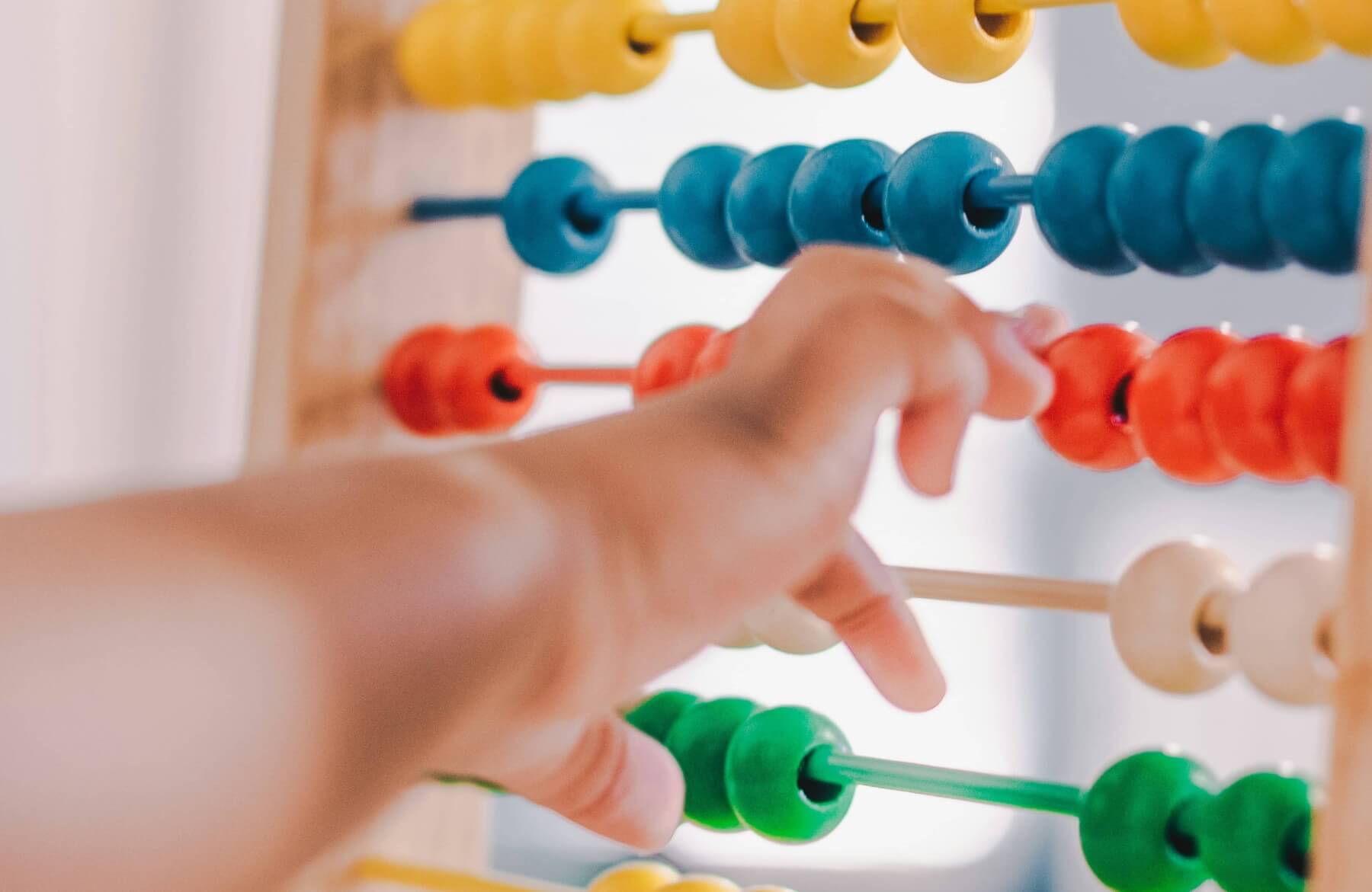 Close up of a colourful abacus with a child's arm reaching to move the counters across.