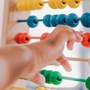 Close up of a colourful abacus with a child's arm reaching to move the counters across.