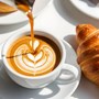 latte being poured into a cup next to a croissant