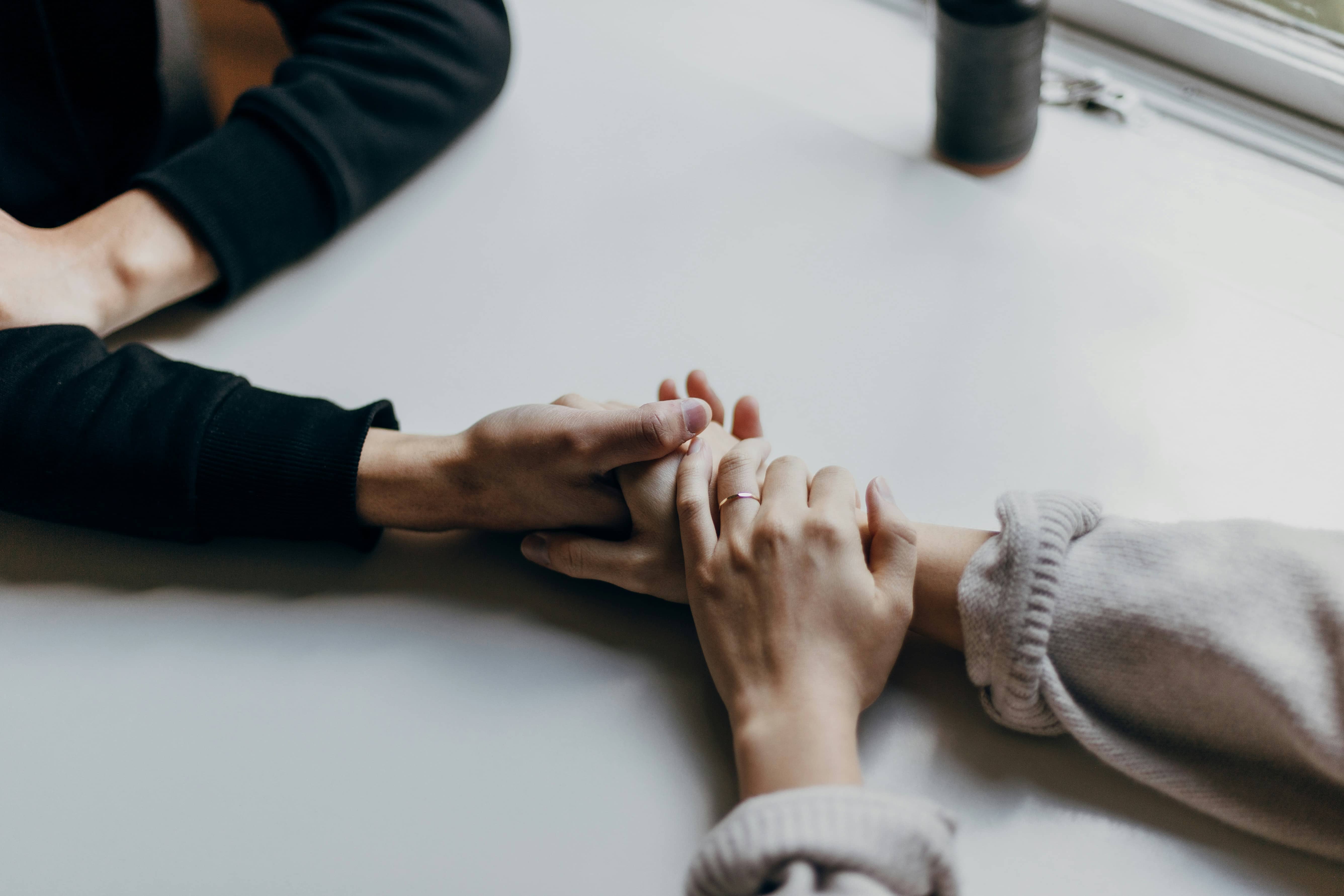 Two people holding hands across a table in a supportive embrace.
