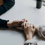 Two people holding hands across a table in a supportive embrace.