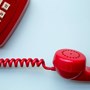 Retro red telephone with a coiled cable on a pale blue background. 
