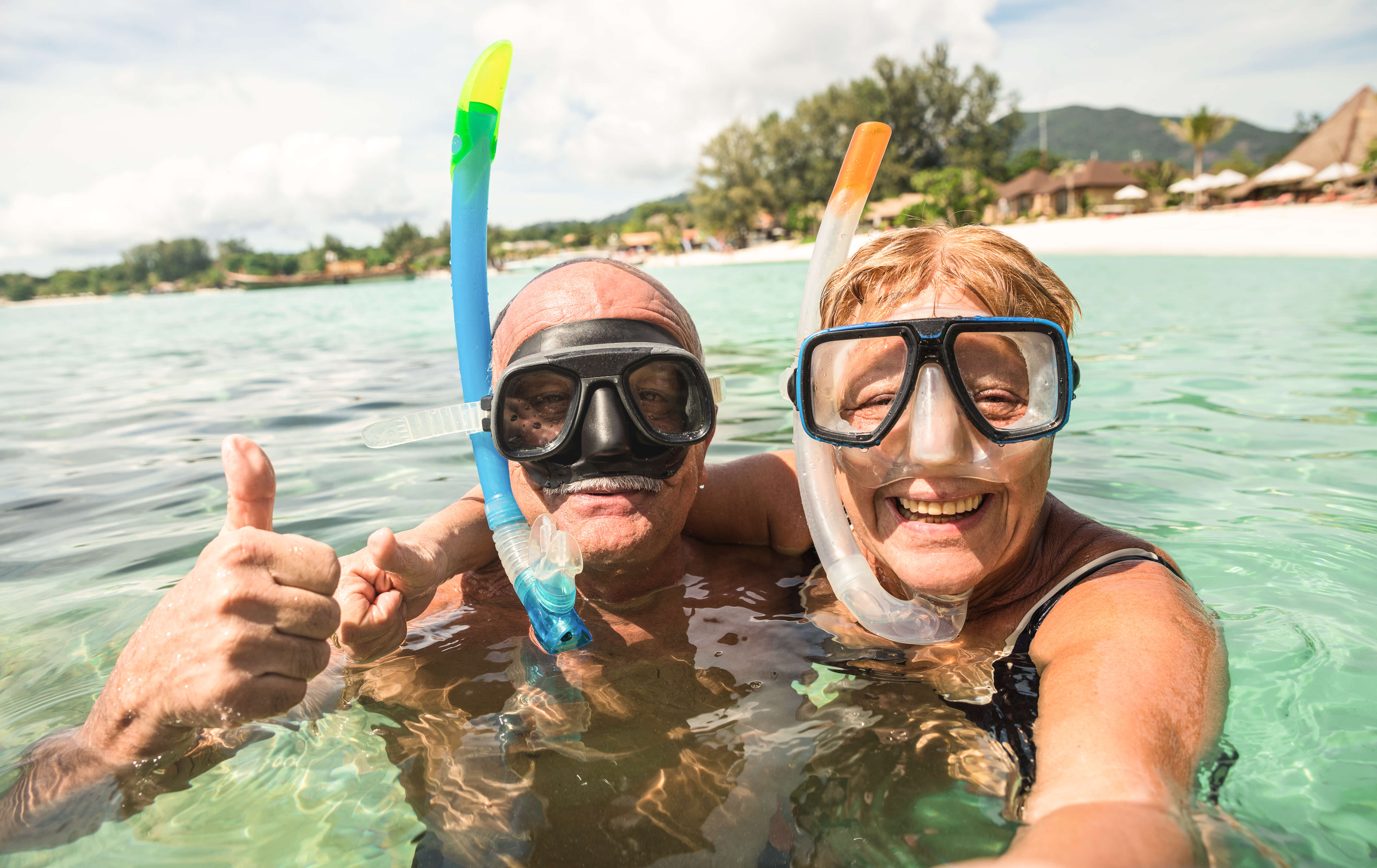 An older couple in the ocean wearing snorkels, giving the camera a thumbs-up | wealthify.com