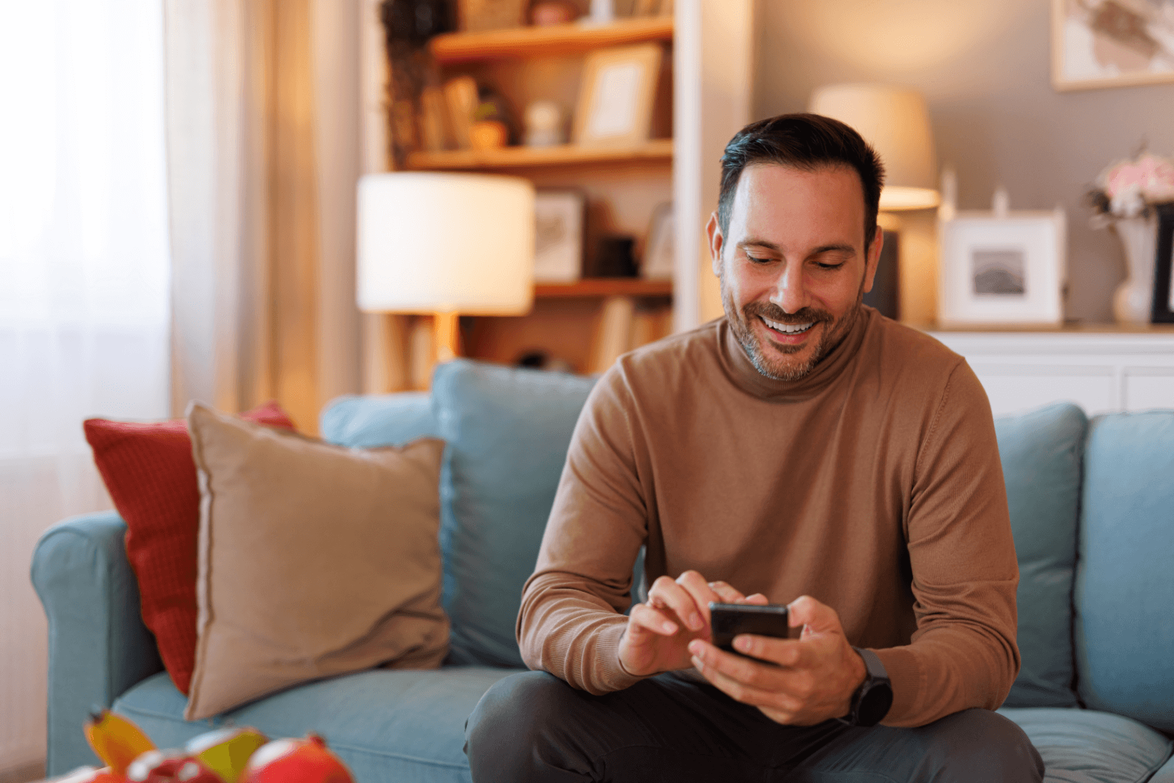 A man sat on his sofa, looking down at his phone and smiling