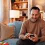 A man sat on his sofa, looking down at his phone and smiling 